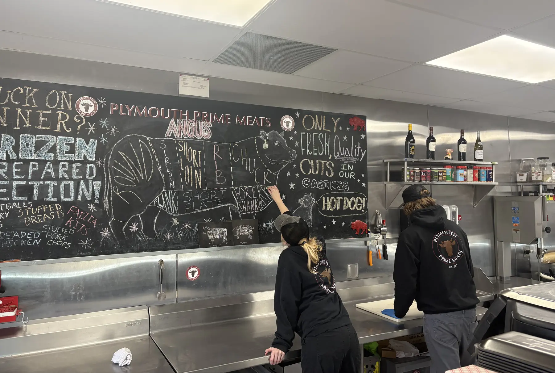 Plymouth Prime Meats staff at the chalkboard beef cut chart behind the counter