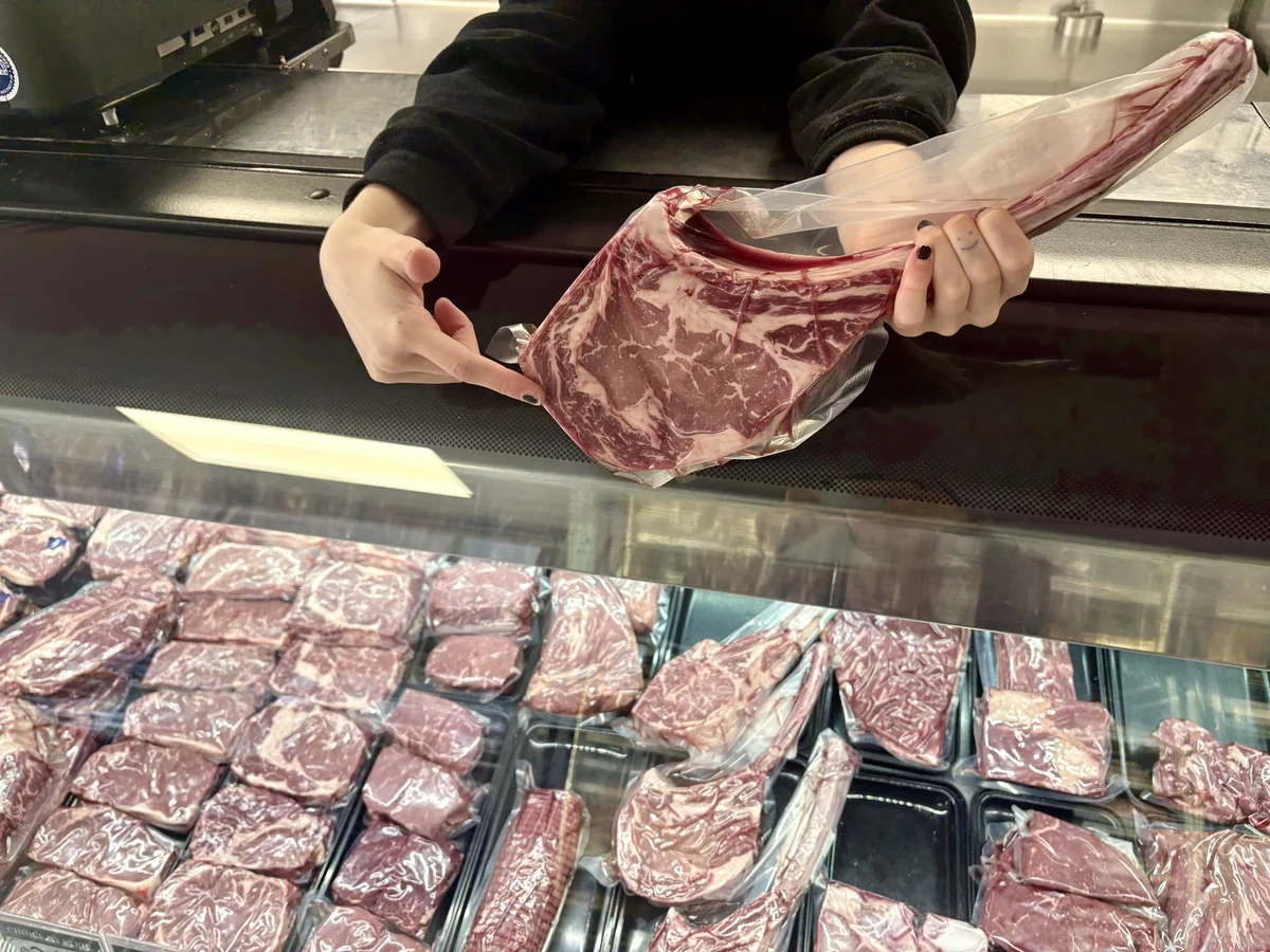 A butcher holds a vacuum-sealed prime rib over the display case