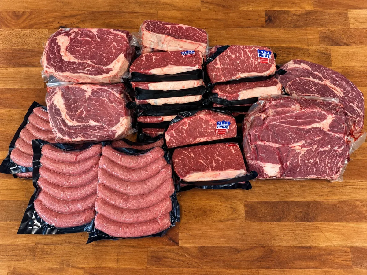 Bulk steaks and sausage laid out on a wood board